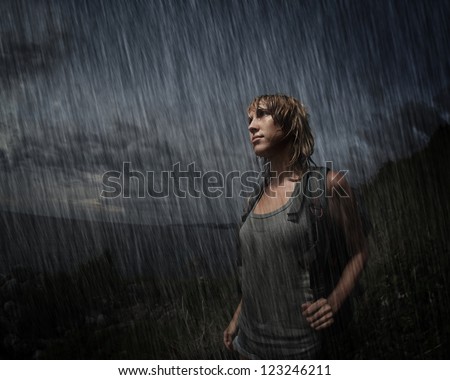 Woman with backpack and wet face, hair and wet closing standing in the midst of darkness. Artificial rain added