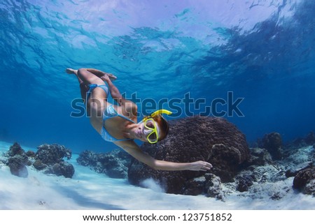 Underwater shoot of a woman swimming over sandy sea bottom