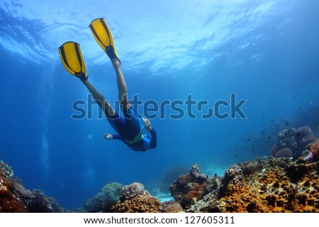 Underwater shoot of a young lady snorkeling and diving on a breath hold over vivid coral reef of tropical island