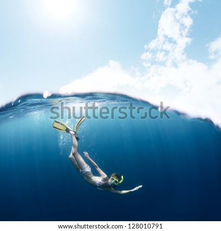 Young lady snorkeling and diving on a breath hold in a clear tropical sea with blue sky with sun and clouds on a surface