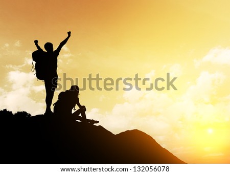 Silhouettes of two hikers with backpacks enjoying sunset view from top of a mountain