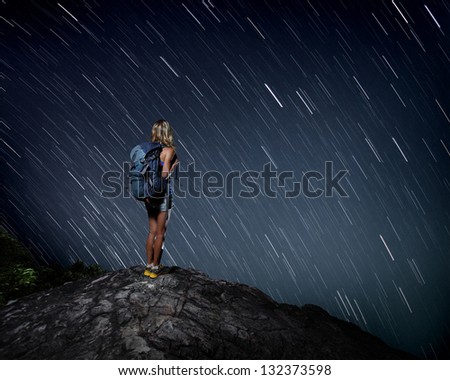 Tourist with backpack standing on top of a mountain and enjoying night sky view with stars