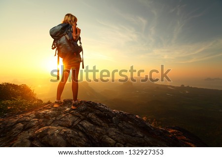 Hiker with backpack relaxing on top of a mountain and enjoying sunrise
