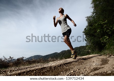 Young lady running along rural road. There is expression of efforts on the face