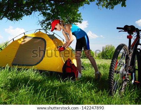 Young sporty lady setting up a tent in a meadow under big oak\'s brunch