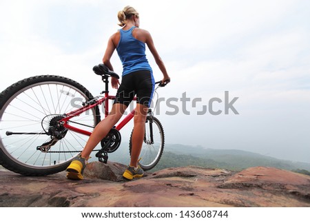 Young sporty lady standing with bicycle on top of a mountain