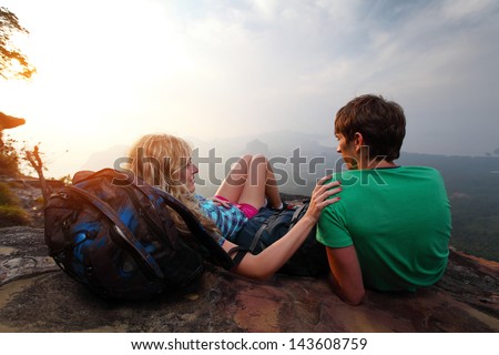 Young hikers relaxing on top of a mountain and enjoying sunrise