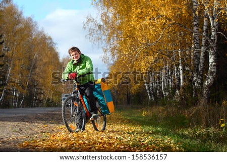 Bicycle tourist with loaded bike relaxing on an autumn road after riding