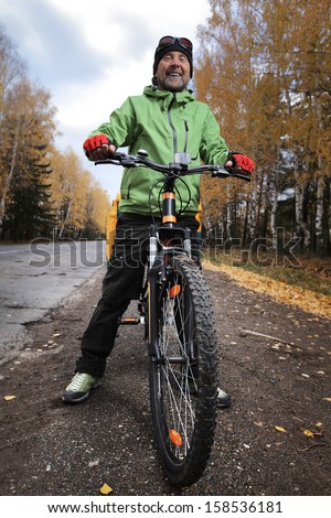 Mature bicycle tourist with loaded bike relaxing on an autumn road after riding