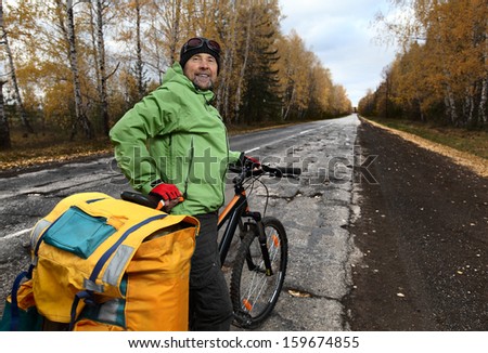 Mature bicycle tourist with his loaded bike on an asphalt autumn road