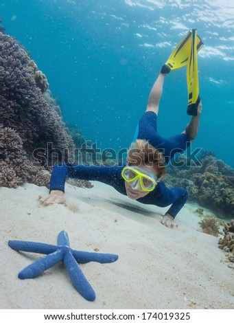 Young woman swimming over sandy sea bottom and watching the blue sea star