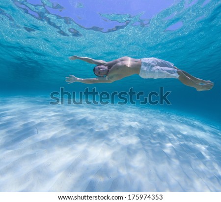 Young man diving on a breath hold in the tropical sea over sandy bottom.