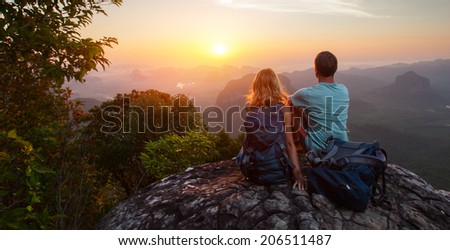 Two hikers relaxing on top of hill and enjoying sunrise over the valley