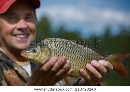 Happy mature fisherman holding his trophy carp (Cyprinus carpio). Focus on the fish