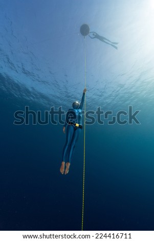 Lady free diver ascending along the rope linked to the buoy on surface. Free immersion discipline