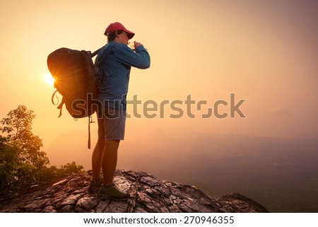 Hiker with backpack drinking water on top of the mountain.