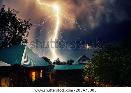 Thunderbolt over the house with dark stormy sky on the background and moon shining through the cloud