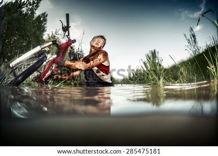 Young man athlete with dirty stained clothes pulling his bicycle from the swamp