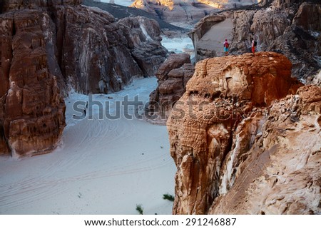 Hikers in the rocky canyon in the desert. Two persons on top of the cliff and another two in the valley. Sinai, Egypt