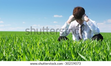 Young sad businessman sitting on green grass