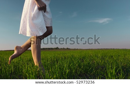 Young woman in white dress walking on meadow with green grass