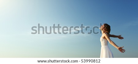Young woman in white dress over blue sky background enjoying the sun