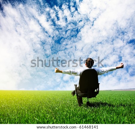 Man with raised hands sitting on chair on green meadow