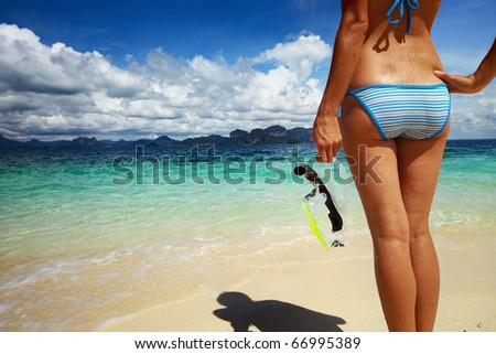 Young woman with wet skin and with a mask standing on sand and going to snorkeling in clear sea