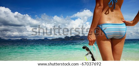 Young woman with wet skin and with a mask standing on sand and going to snorkeling in clear sea
