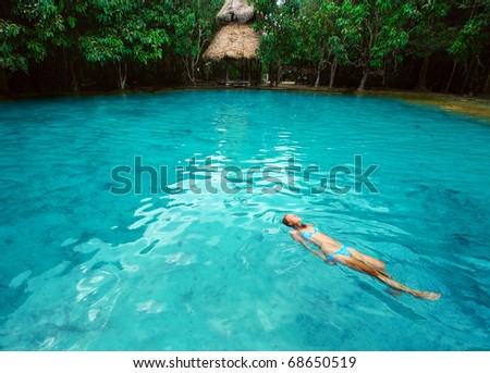 Young woman swimming alone in a blue clear water of a lake situated in tropical forest