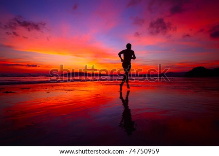 Young men jogging on wet sand by sea edge on vivid sunset background