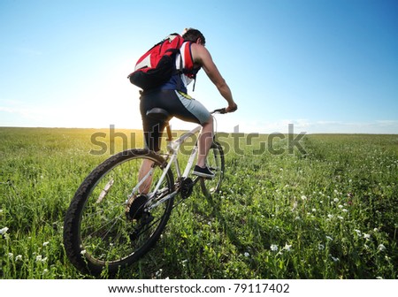 Young man riding on bicycle through deep grass with red backpack