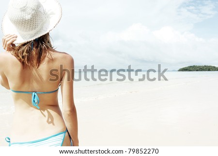 Young woman in straw hat standing by blue sea and looking to horizon