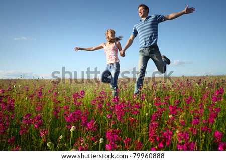 Young man and woman running on countryside meadow with pink flowers