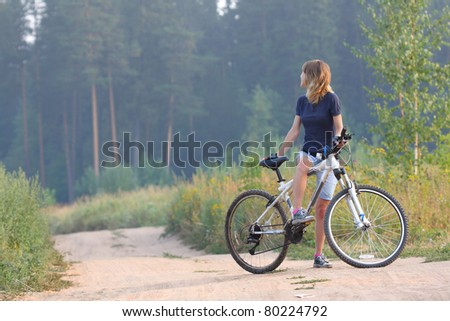 Young woman standing with bicycle on rural countryside road and looking back