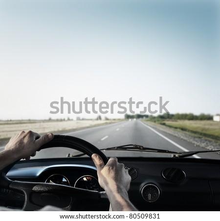 Driver\'s hands on a steering wheel of a retro car during riding on an empty asphalt road