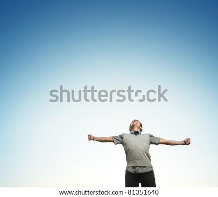 Young happy man on blue sky background with raising hands and looking to a sky