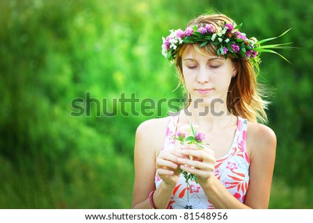 Young smiling woman with wreath holding a clover flower on green background