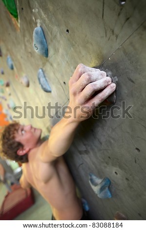Young man climbing indoor wall. Focus on a fingers