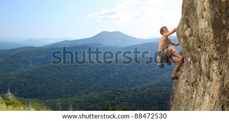 Young man climbs on a rocky wall in a valley with mountains