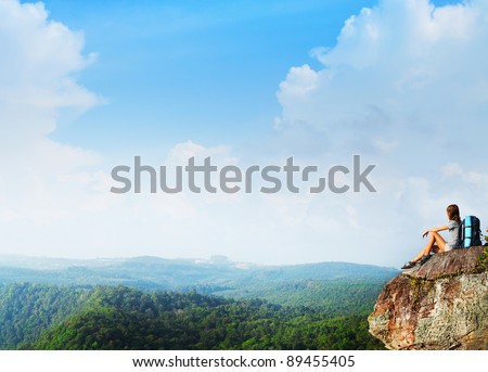 Young woman with backpack sitting on a rock and looking to the horizon