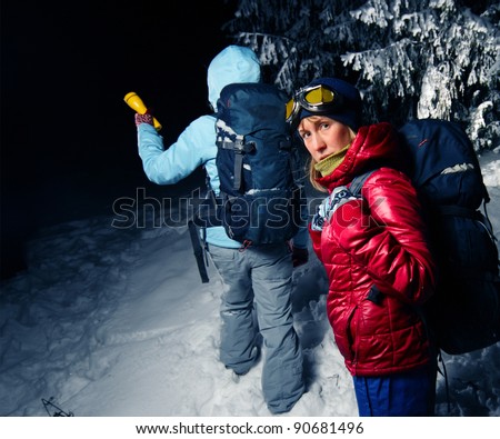 Women with backpacks exploring deep wild forest at night with a torch