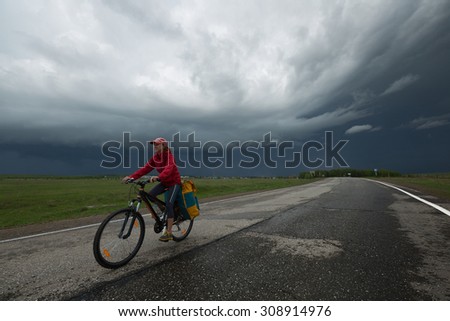 Lady cycling on the paved road with storm clouds on the background