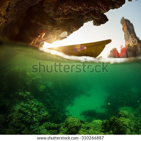 Lady paddling kayak in the tropical sea near the rock with underwater view of the coral reef