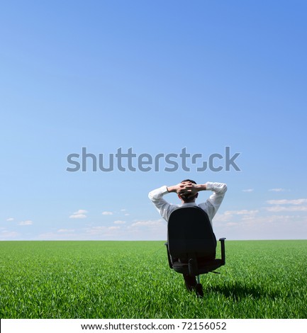 Businessman sitting on chair in green meadow and looking to a blue clear sky 商業照片 © 