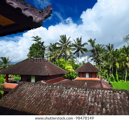 Group of bungalows with traditional Balinese roofs in green tropical garden in sunny day