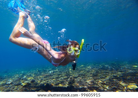 Young woman diving on a breath hold and making bubbles over coral reef in blue transparent sea