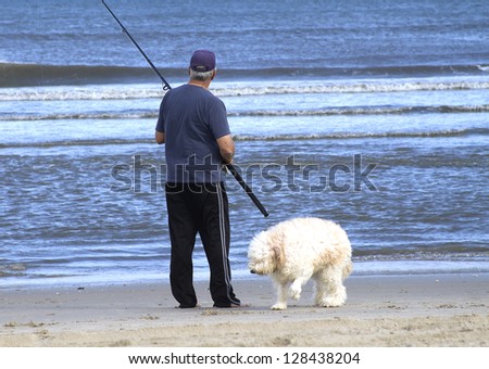 Man fishing in late afternoon with large shaggy dog beside him exploring the shoreline