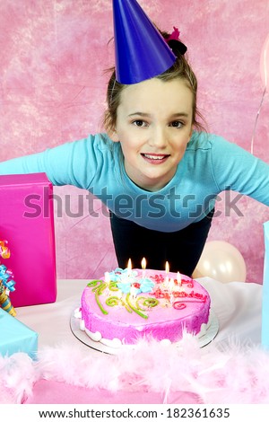 Girl\'s birthday party celebration with cake and balloons with girl excited to blow out candles