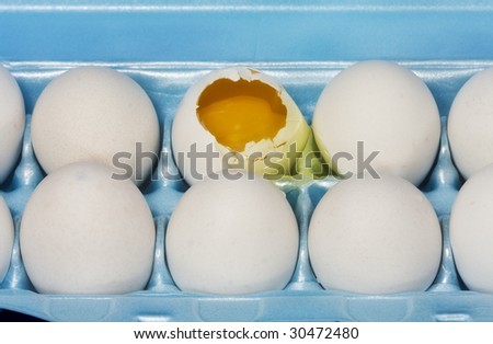 Closeup on eggs in carton with one egg broken and yolk showing